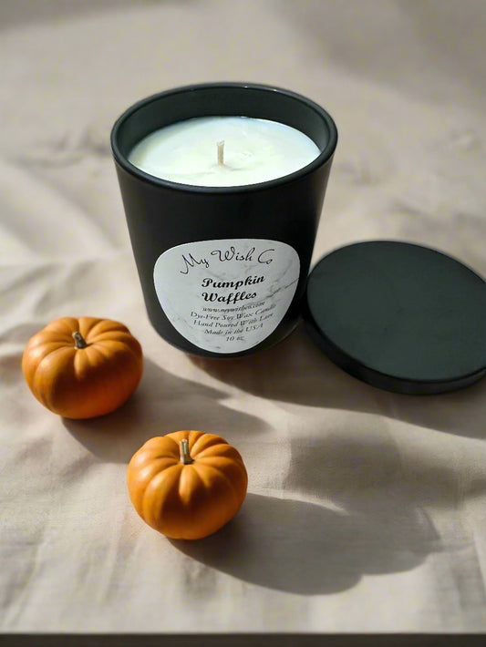Black candle labeled 'Pumpkin Waffles' with two small pumpkins on a light background
