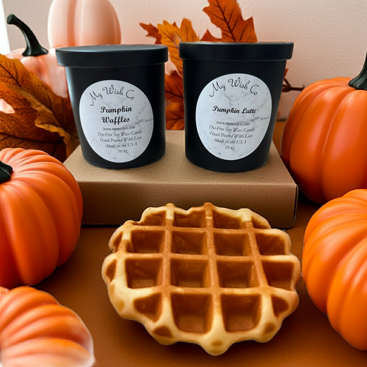 Two black containers labeled 'Pumpkin Waffles' and 'Pumpkin Latte' with a waffle on a table surrounded by pumpkins and fall leaves.