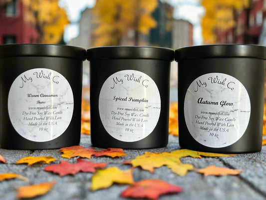 Three black candles with labels on a surface with autumn leaves 
