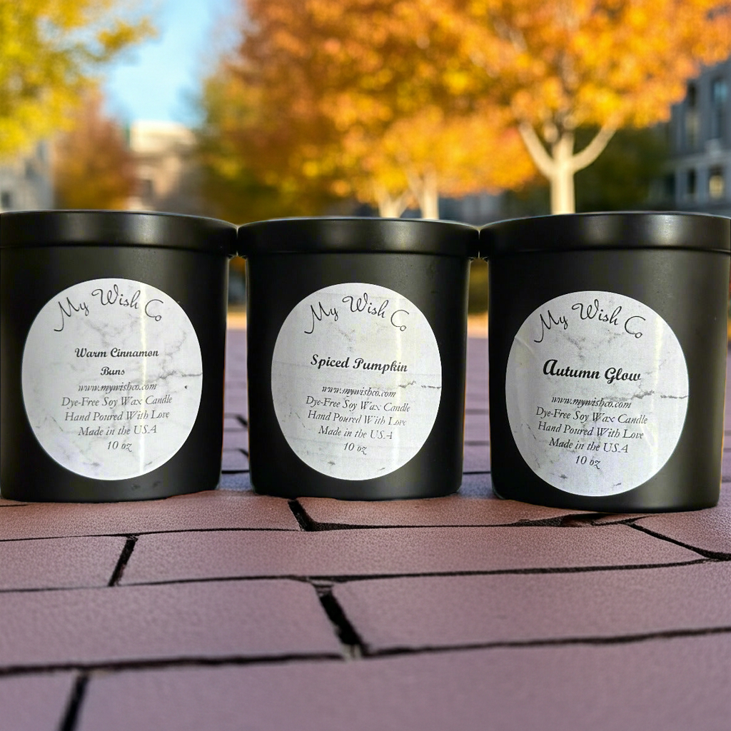 Three black candles with labels on a brick surface with autumn trees in the background