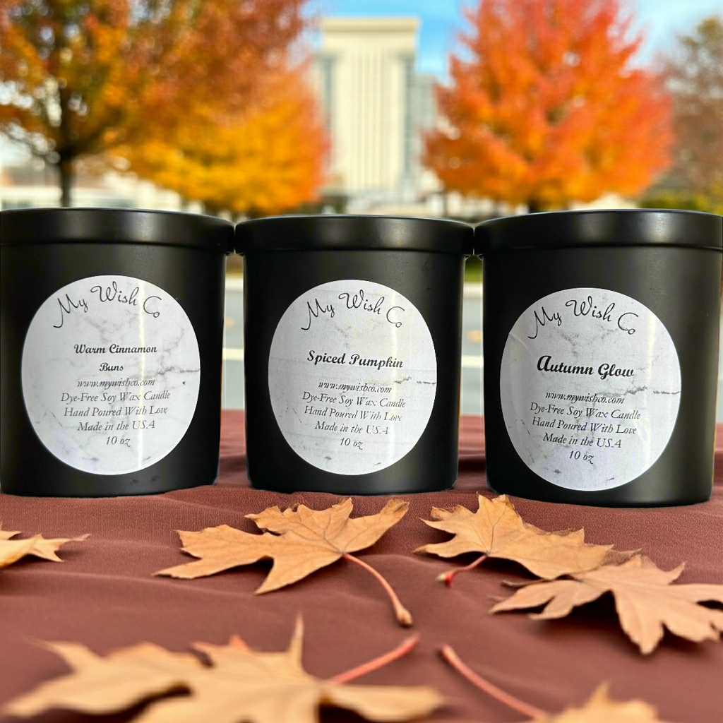 Three black candles labeled 'My Wish Co' with autumn leaves on a table.