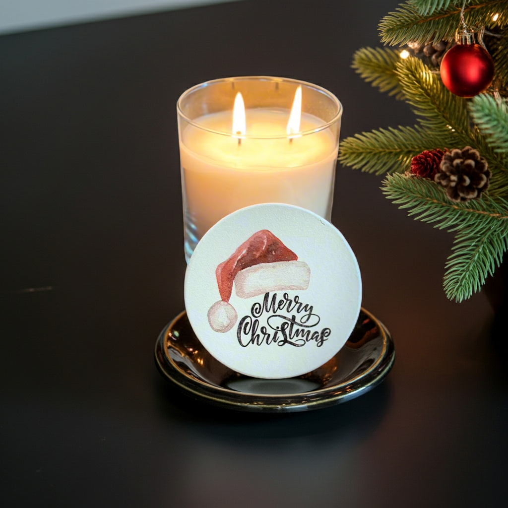 Candle with a 'Merry Christmas' coaster on a dark surface with Christmas decorations.