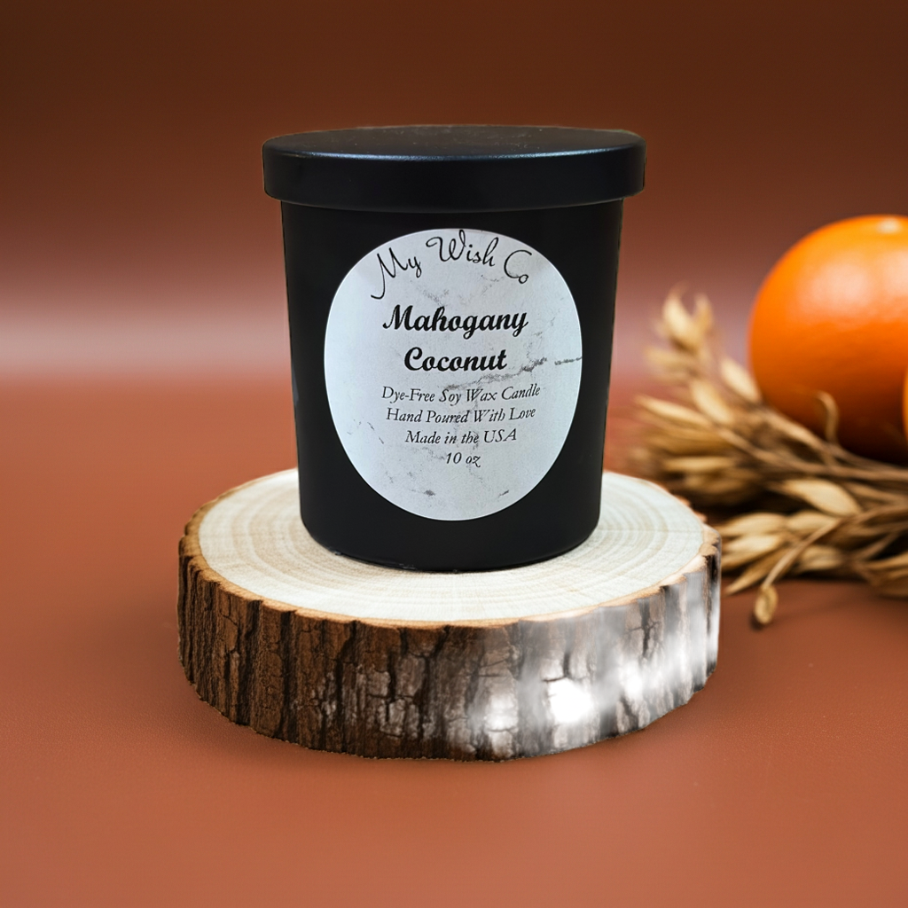 Candle labeled 'Mahogany Coconut' on a wooden stand with a blurred background