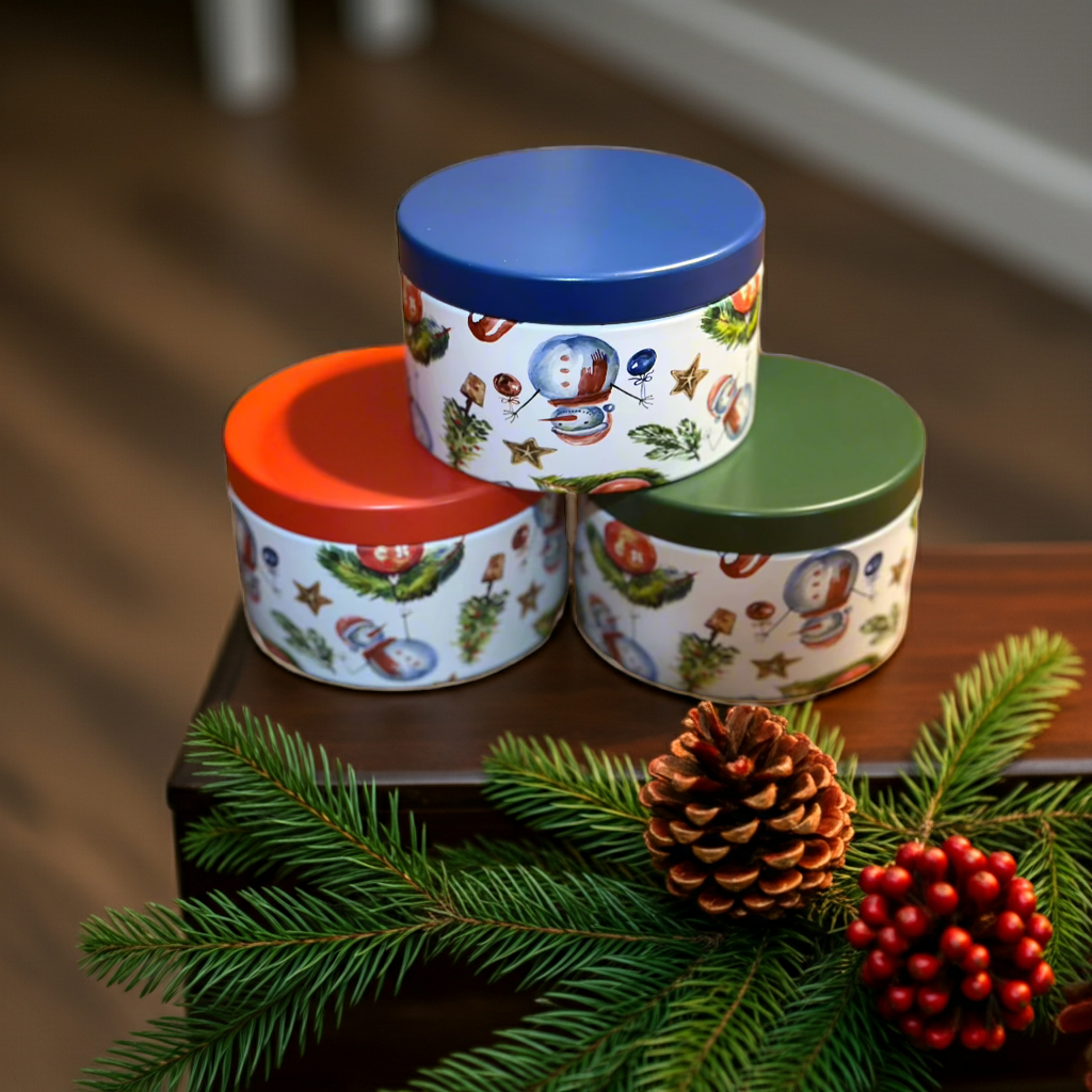 Three decorative tins with colorful lids on a wooden surface with Christmas decorations.