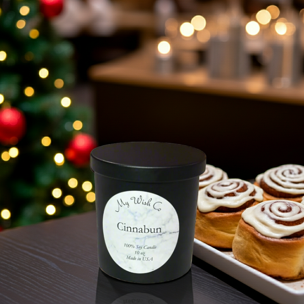 Black candle labeled 'Cinnabun' with a Christmas tree and cinnamon rolls in the background