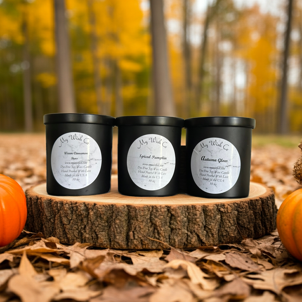Three black candles with labels on a wooden stump in an autumn setting with pumpkins and leaves.