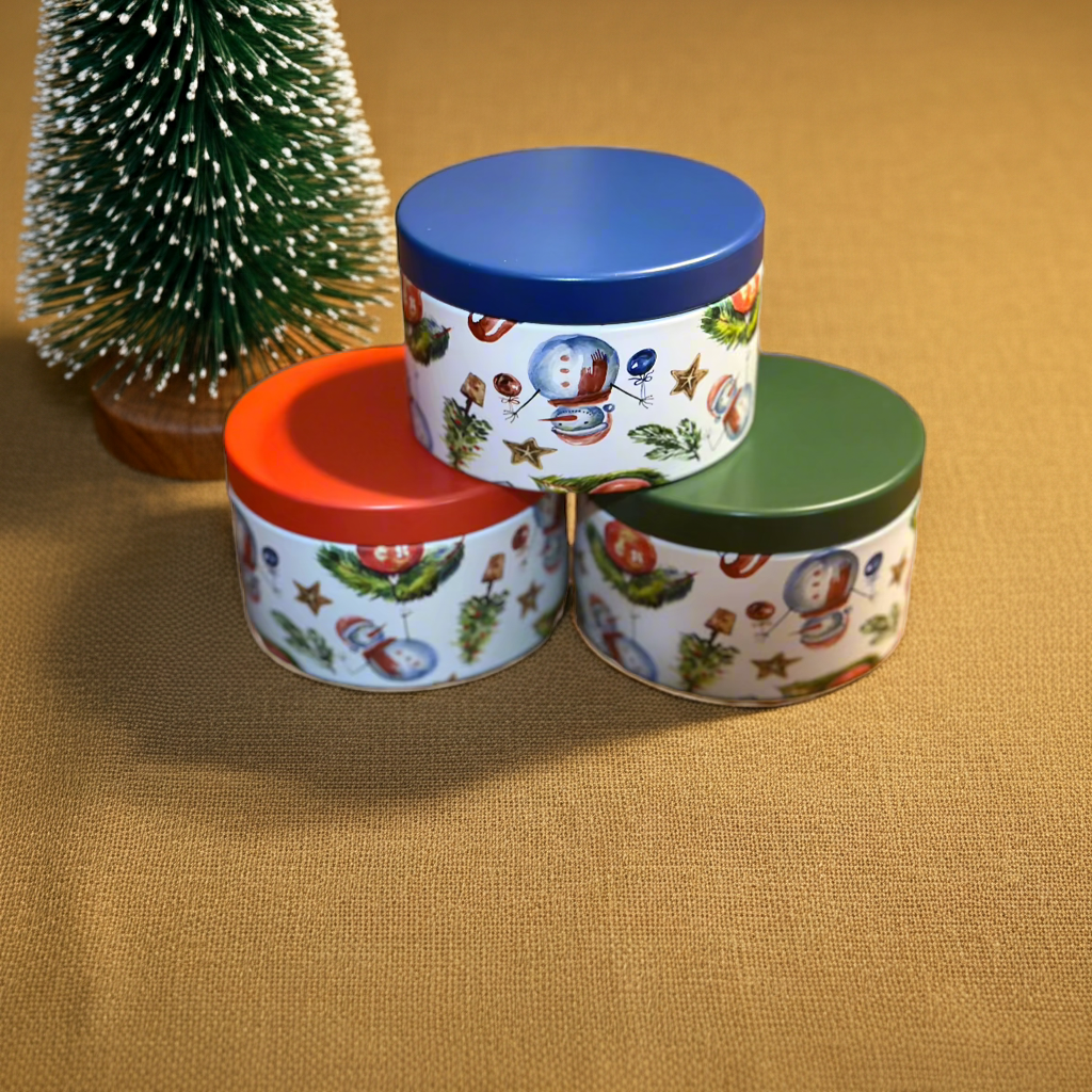 Three cylindrical containers with colorful lids on a textured surface with a small Christmas tree.