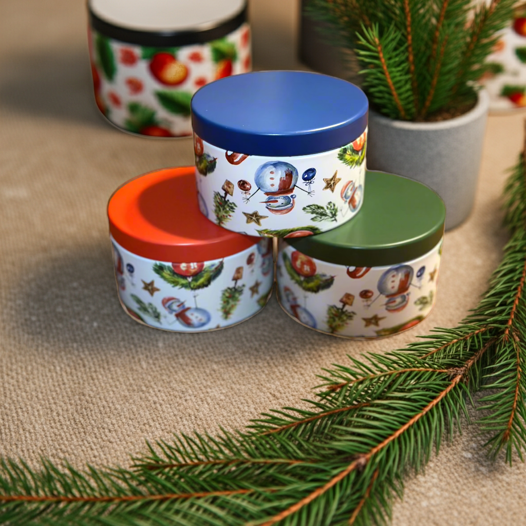 Three decorative tins with colorful lids on a textured surface with Christmas tree branches.