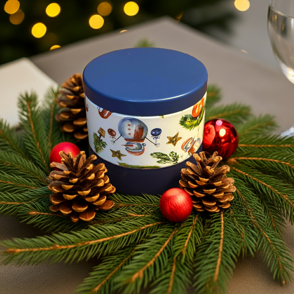 Decorative candle with festive design surrounded by pine cones and red ornaments on a table.