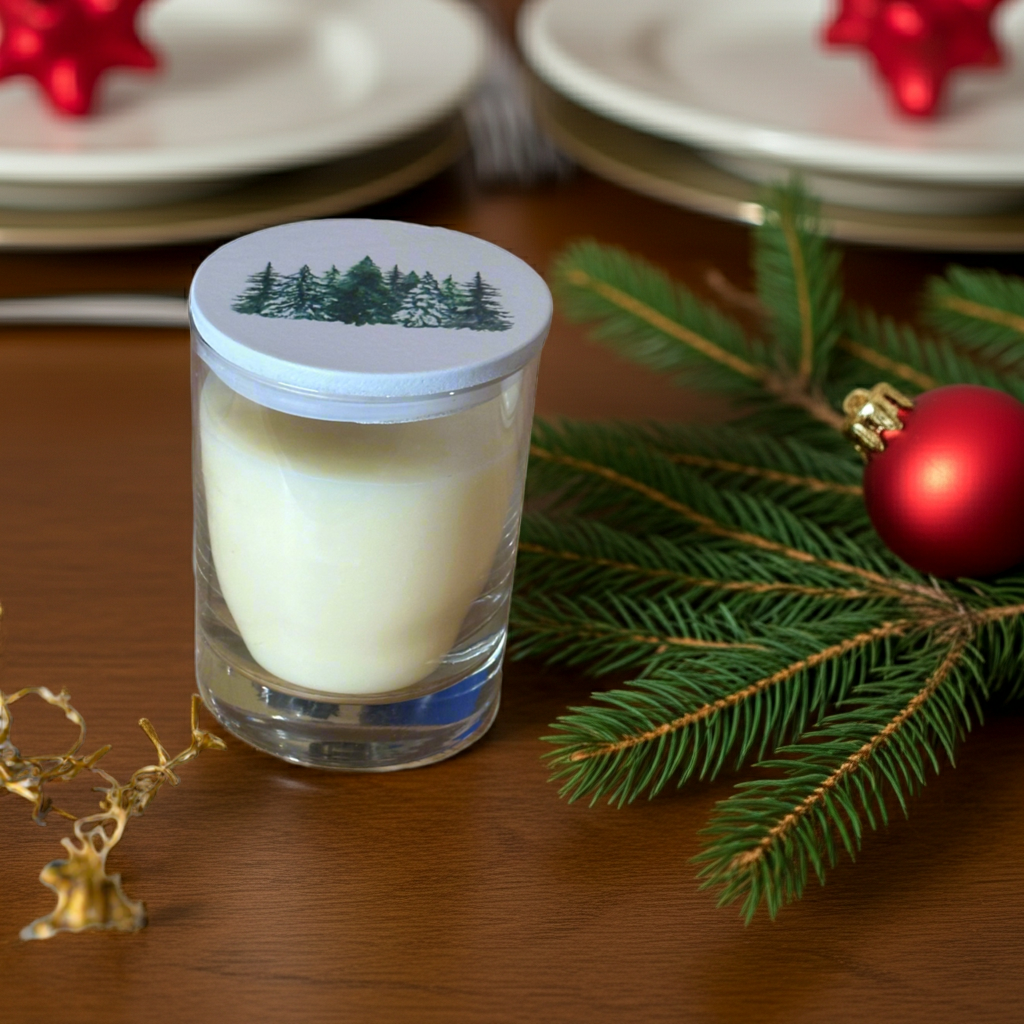 Glass candle with a lid featuring a forest design, surrounded by Christmas decorations on a wooden surface.